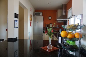 A kitchen with a refrigerator, microwave, and a fruit display.