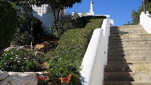 Un escalier en pierre menant au sommet d’une colline, entouré de verdure et bordé de murs blancs.