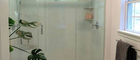 A glass-enclosed shower with a white tiled wall, a window, and a towel rack.