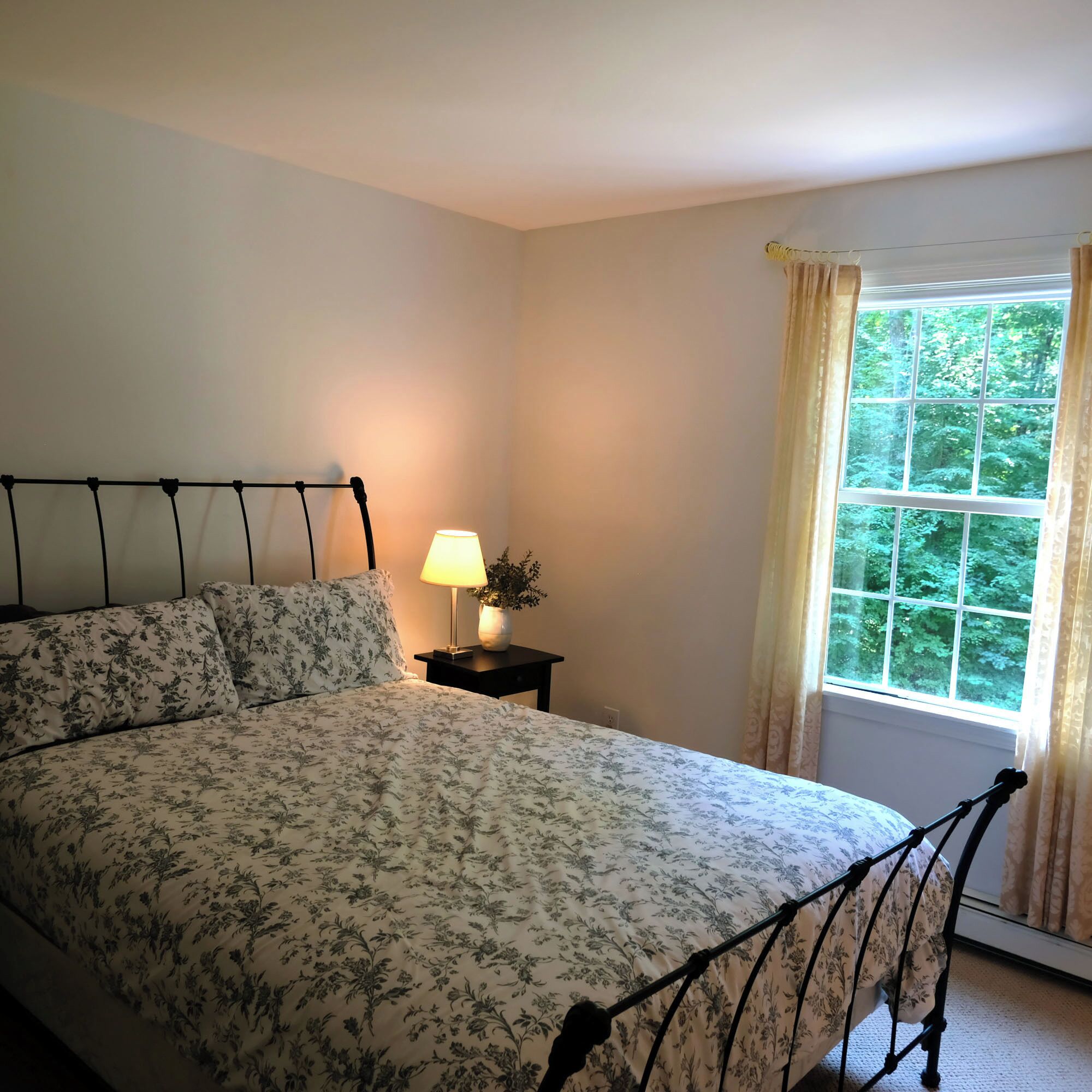 Een slaapkamer met een bed, een nachtkastje met een lamp en een raam met gordijnen.