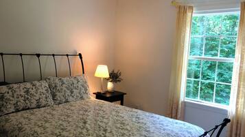 Een slaapkamer met een bed, een nachtkastje met een lamp en een raam met gordijnen.
