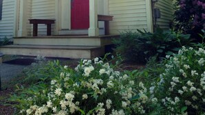 A house with a red door, a porch with two benches, and a garden with white flowers. - Cheerful 3-bedroom cottage with woodstove (Sheffield)