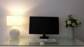 A desk with a computer monitor, keyboard, and mouse. There is a lamp and a vase with flowers on the desk.