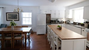 A kitchen with wooden countertops, white cabinets, a dining table with chairs, a refrigerator, and a chandelier. - Cheerful 3-bedroom cottage with woodstove (Sheffield)