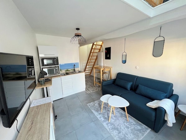 A compact living space with a kitchenette, a sofa, a TV, and a ladder leading to a loft area. - COSY CASA. (Abbeville)