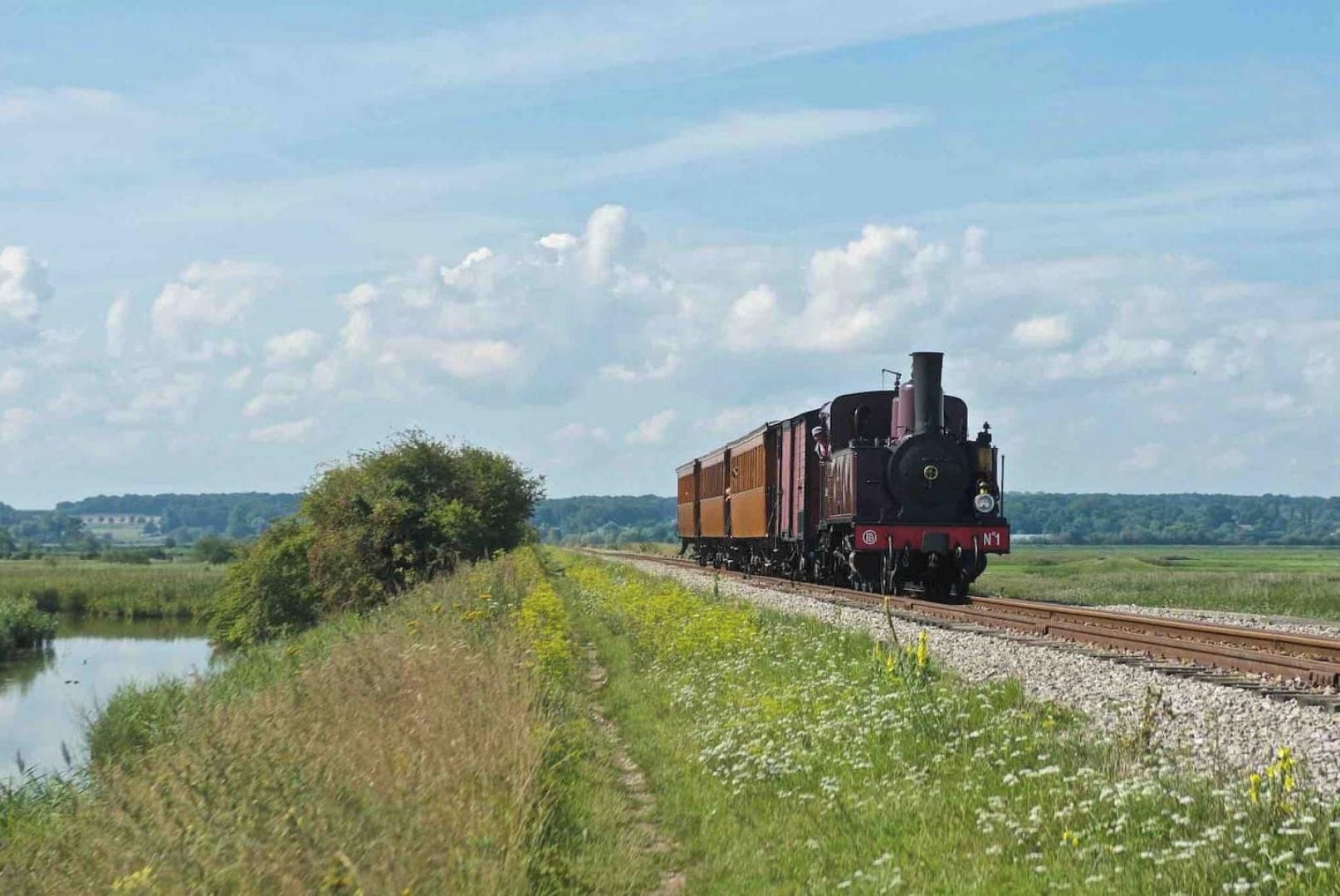A steam locomotive on a railway track with a rural landscape in the background.