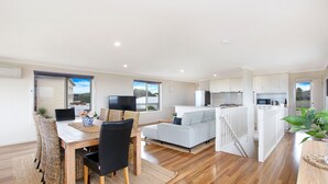 Un espace de vie moderne et ouvert, comprenant un coin repas, un canapé gris, une cuisine et un balcon avec vue.