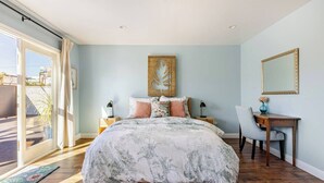 Ein Schlafzimmer mit einem großen Bett, einem Schreibtisch, einem Stuhl, einem Spiegel und Blick ins Freie.