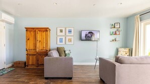 Ein Wohnzimmer mit Fischgrätparkett, einem Holzschrank, zwei grauen Sofas und einem Fernseher an der Wand.