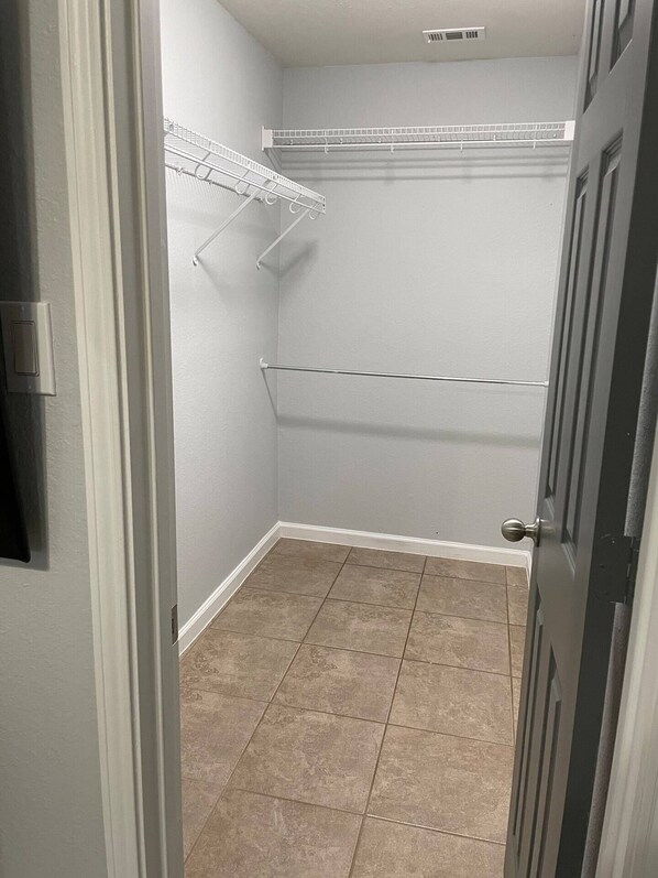 A walk-in closet with white walls, a tiled floor, and metal shelving units.