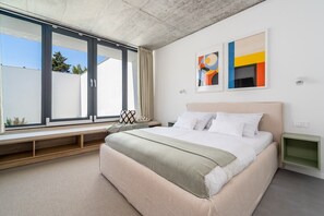 Ein modernes Schlafzimmer mit einem großen Bett, einer Sitzbank am Fenster und abstrakter Wandkunst.