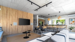 Una sala de estar moderna con un televisor grande, un comedor y una cocina al fondo.