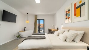 Una habitación de hotel moderna con una cama grande, un escritorio, una bañera y un televisor en la pared.