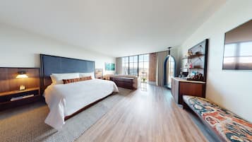 Habitación de hotel moderna con una cama grande, un sofá, un escritorio y vistas a la ciudad a través de amplias ventanas.