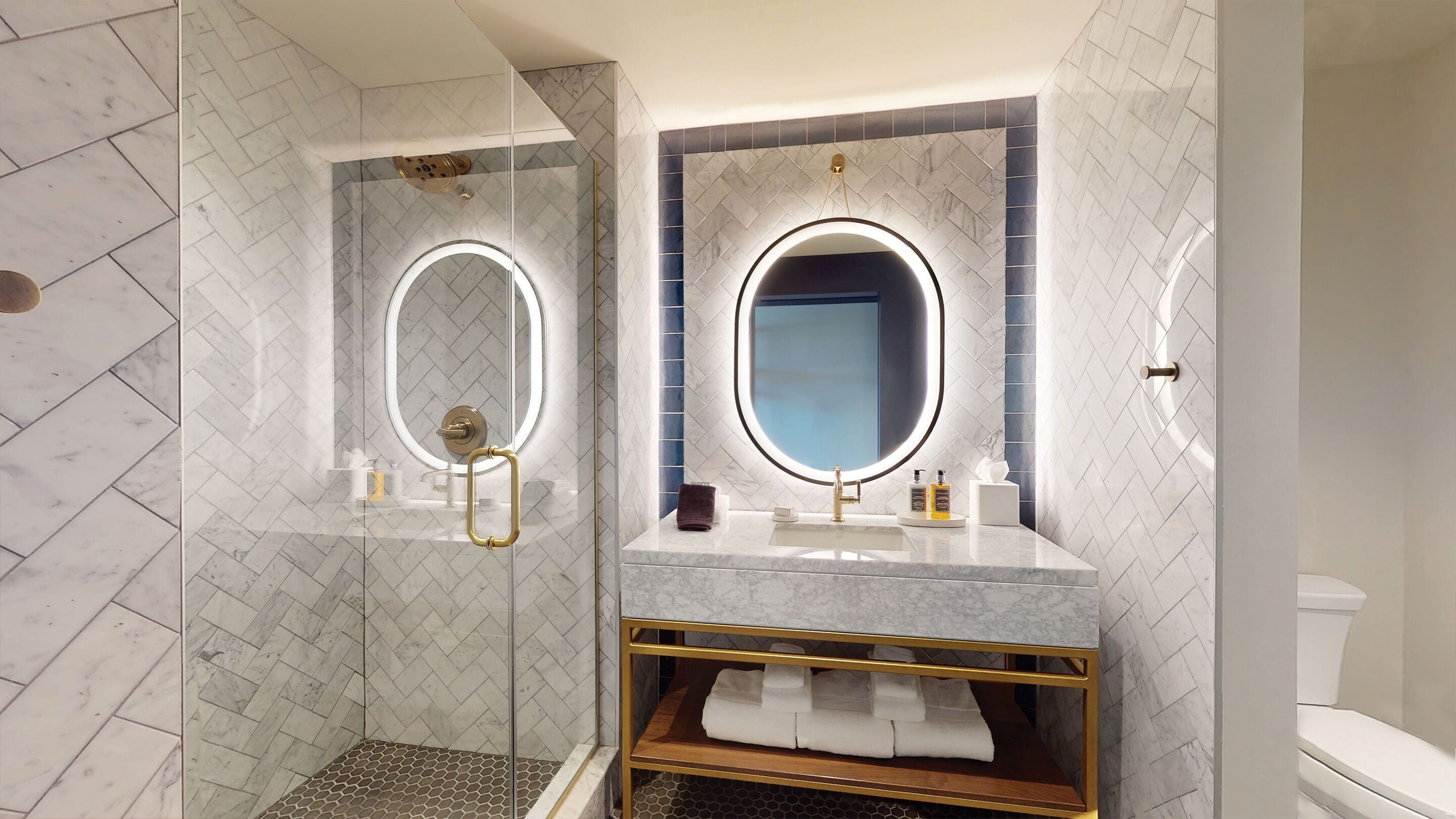 A modern bathroom with a glass-enclosed shower, a vanity with a gold frame, and two large mirrors with built-in lighting.
