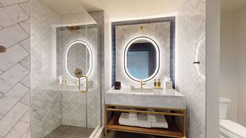 A modern bathroom with a glass-enclosed shower, a vanity with a gold frame, and two large mirrors with built-in lighting.
