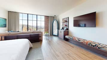 A hotel room with a large window, a sofa, a bed, a TV, and a small table with a plant.