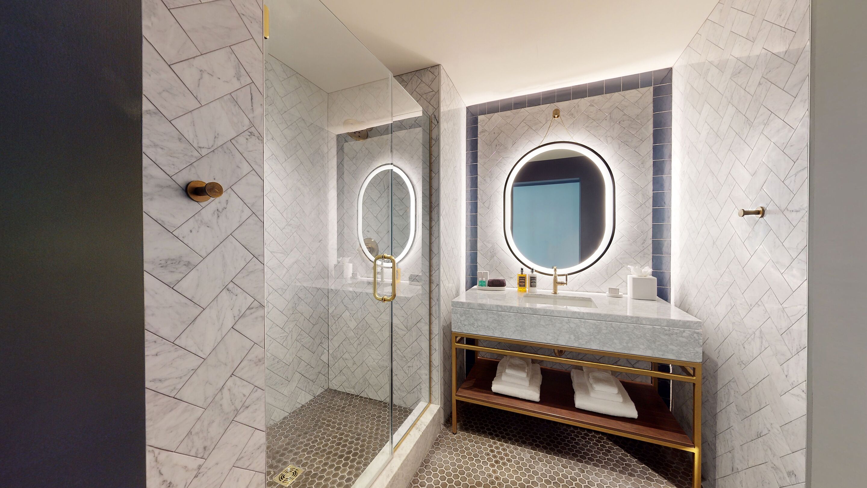 A modern bathroom with a glass-enclosed shower, a vanity with a gold frame, and a large mirror with a circular light.