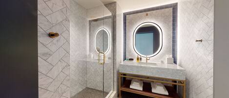 A modern bathroom with a glass-enclosed shower, a vanity with a gold frame, and a large mirror with a circular light.