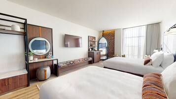 Habitación de hotel con dos camas, televisor, espejo, escritorio pequeño y pared decorativa de ladrillo.
