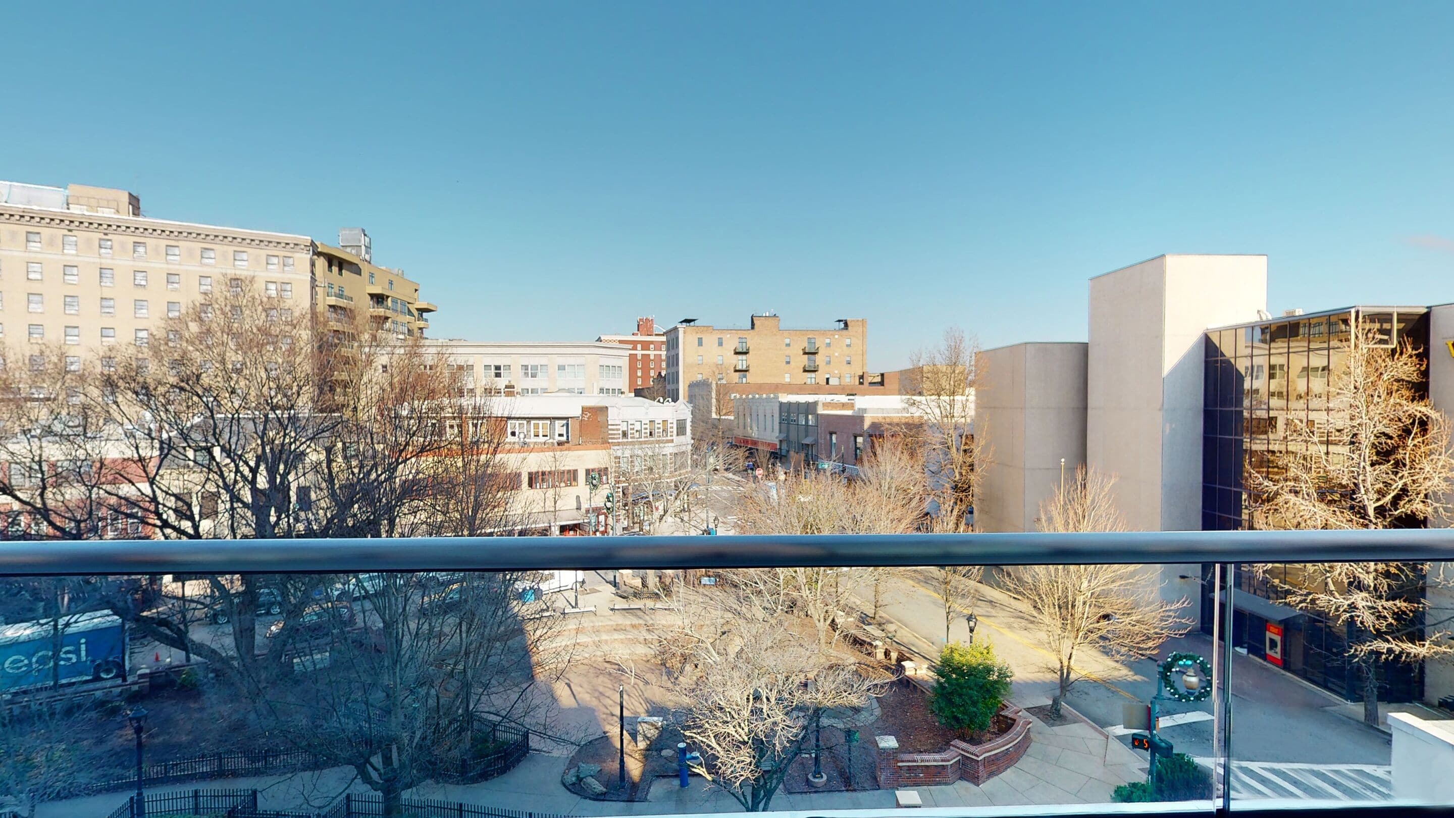 A cityscape with modern buildings, a clear sky, and a park area with bare trees.