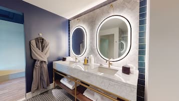 A modern bathroom with dual sinks, a robe rack, and two large mirrors with illuminated frames.
