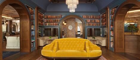 Una biblioteca con un sofá amarillo grande, estanterías de madera y una lámpara de araña.
