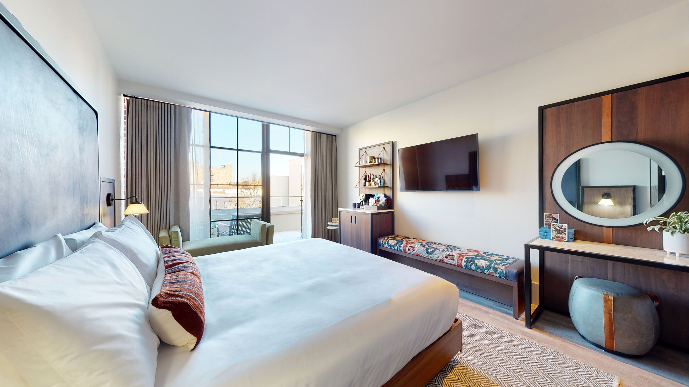Una habitación de hotel moderna con una cama grande, una zona de estar, televisor y vistas a la ciudad.