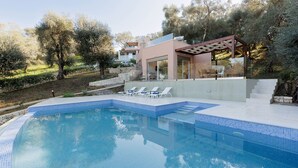 Et moderne poolområde med klart, blåt vand, en pergola og en trappe op til en bygning.