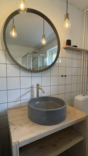 Une salle de bain avec un miroir rond, un lavabo rond et deux lampes suspendues.