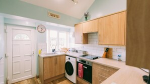 A compact kitchen with wooden cabinets, a washing machine, and a tiled backsplash. - Cozy Scarning Apartment for Two (Dereham)