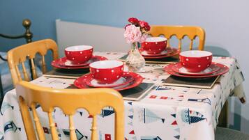 A dining table with red and white polka dot tableware, a vase with flowers, and a tablecloth with nautical patterns.