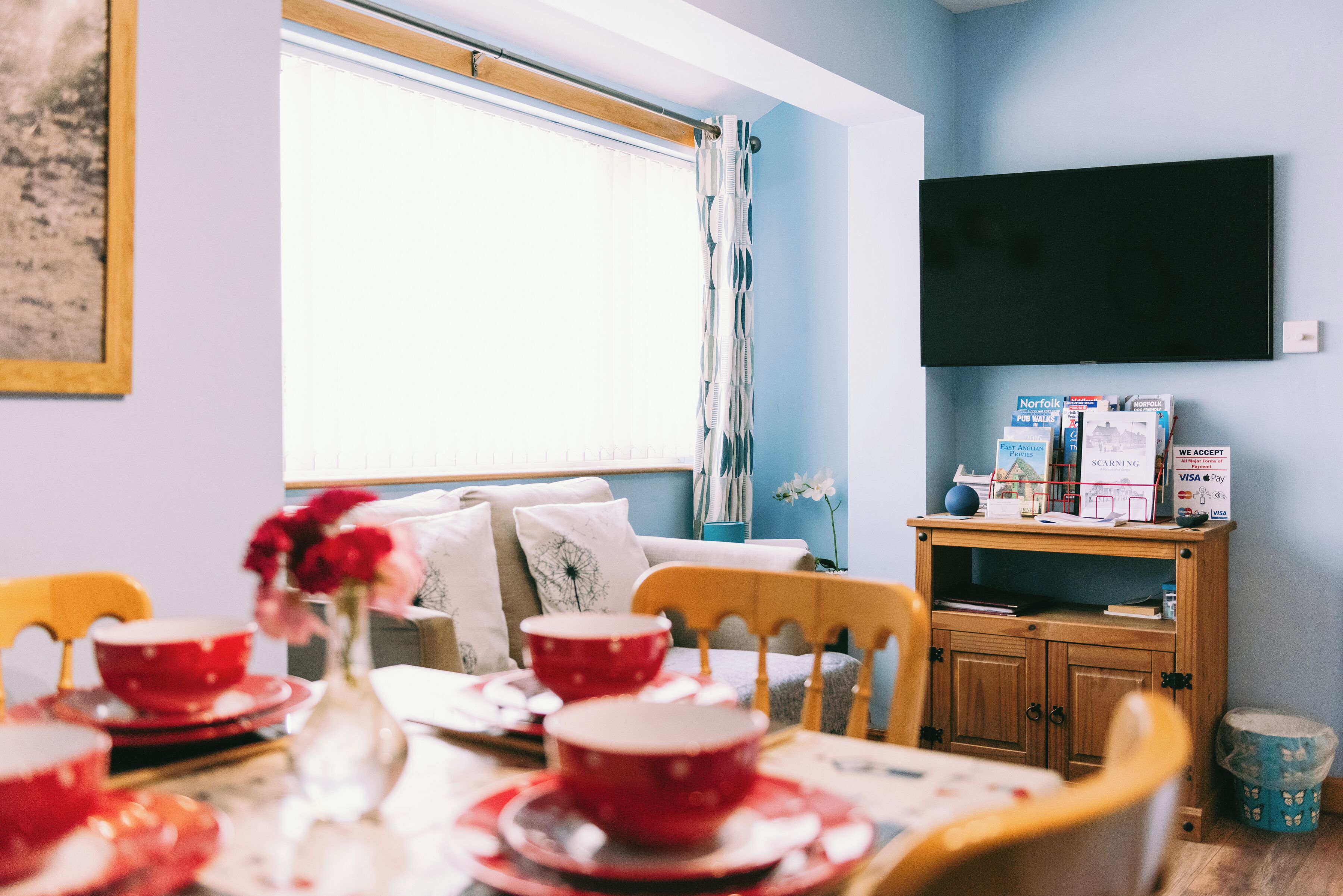 A dining area with a table set for four, a wooden cabinet, and a television mounted on the wall.
