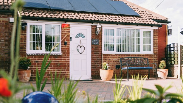 A brick building with a white door, two windows, a bench, and potted plants. - Cozy Scarning Apartment for Two (Dereham)