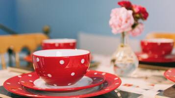 A table with a red polka-dotted cup and saucer, a vase with pink flowers, and a red cup in the background.