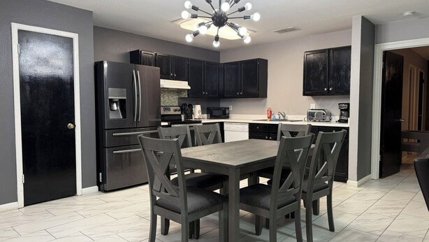 A modern kitchen with dark cabinets, a stainless steel refrigerator, a built-in oven, and a dining area with a wooden table and chairs.