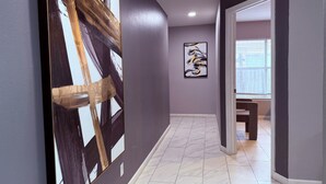 A hallway with a large abstract painting on the left, a smaller piece on the wall, and a door leading to another room.