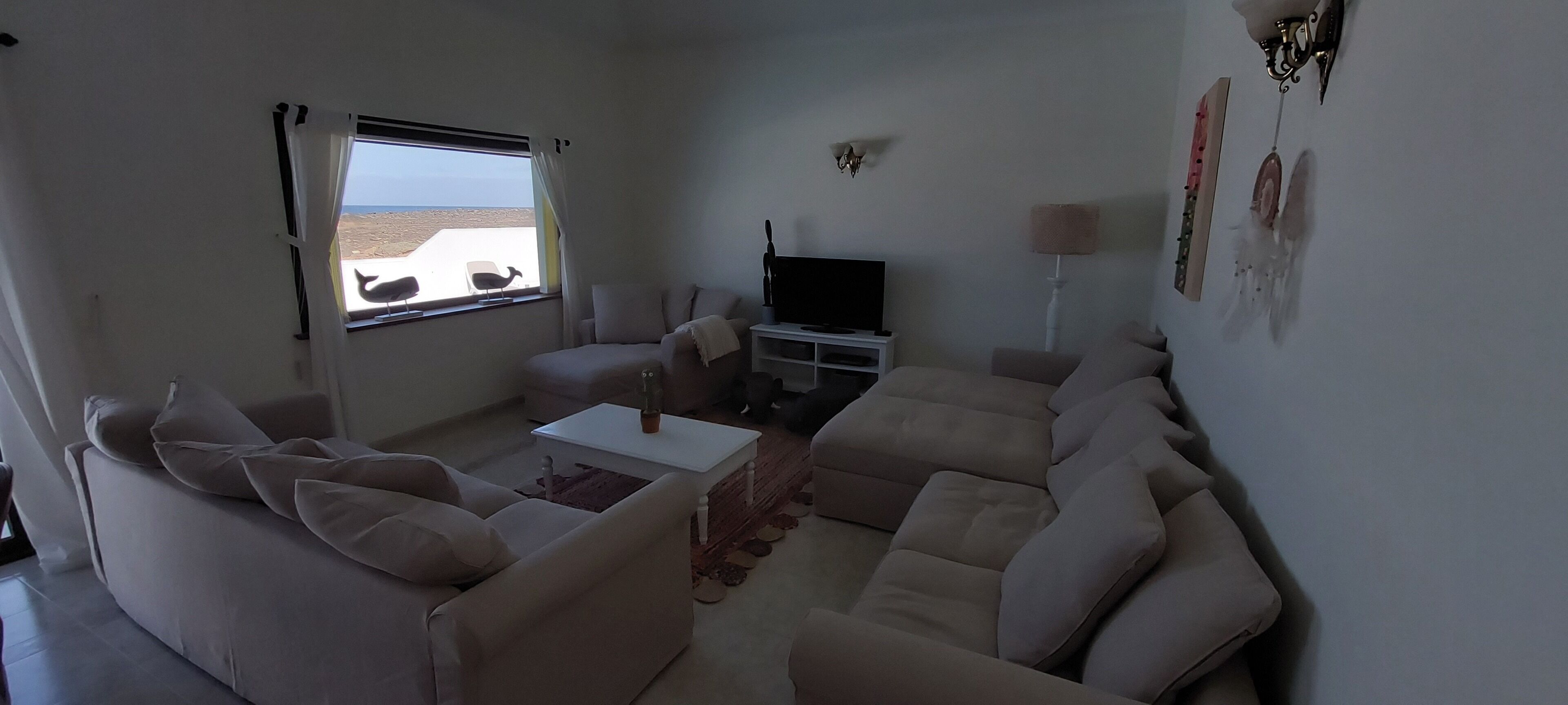 Una sala de estar con un sofá, una mesa de centro, un televisor y una ventana con vista a la playa.