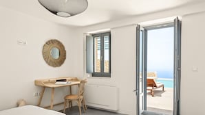 A bedroom with a desk, chair, and a view of the beach through an open door. - Patio Villas (West Mani)
