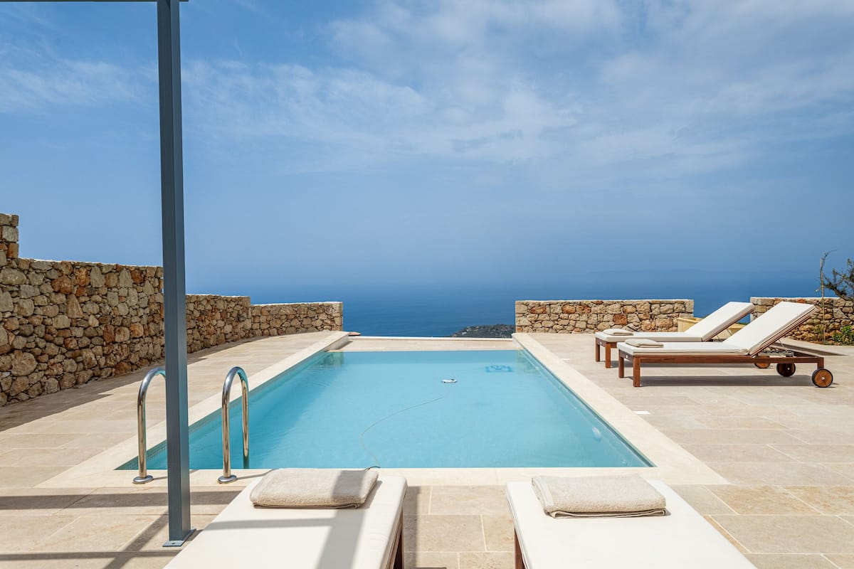 A swimming pool with lounge chairs and a stone wall, overlooking a body of water.