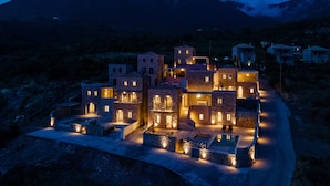 A modern, multi-story building with a pool area, surrounded by a mountainous landscape. - Patio Villas (West Mani)
