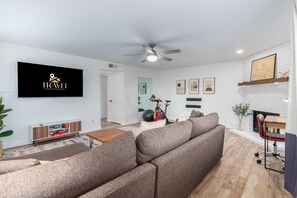A modern living room with a sofa, a ceiling fan, a TV, and a fireplace.