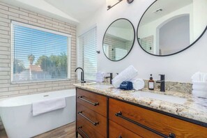 A modern bathroom with a bathtub, vanity, and two round mirrors.
