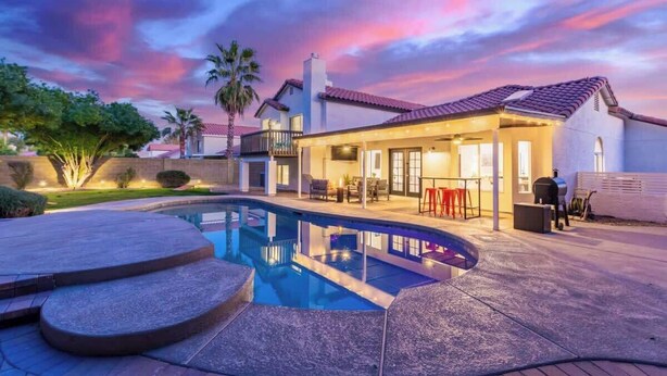 A swimming pool with steps, a covered patio, and a house with a red-tiled roof. - Mesa Getaway | Htd. Pool, Pellet Grill & Patio TV (Mesa)