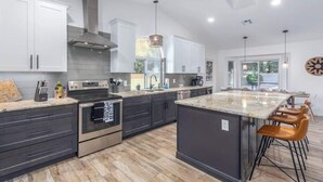 A modern kitchen with dark cabinets, stainless steel appliances, a large island with bar stools, and pendant lighting. - Mesa Getaway | Htd. Pool, Pellet Grill & Patio TV (Mesa)