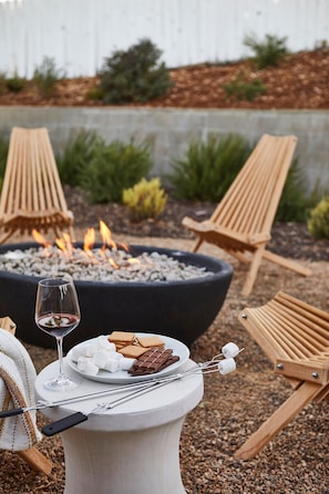 A fire pit with seating and a table with snacks and a glass of wine.
