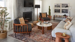 A living room with a fireplace, a sofa, armchairs, a coffee table, and a TV mounted on the wall.