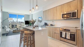 Une cuisine moderne dotée d’un îlot central, de meubles en bois, d’appareils électroménagers en acier inoxydable et offrant une vue sur la ville grâce à de grandes fenêtres.
