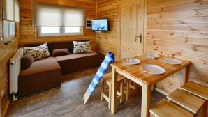 Een houten blokhut interieur met een bank, een eettafel met borden en glazen, en een televisie aan de muur.