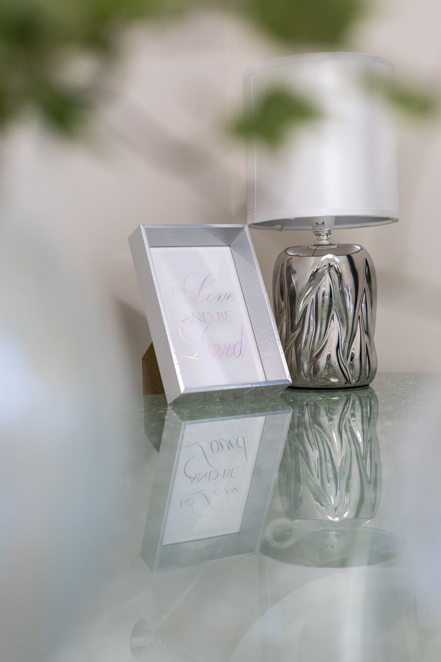 Een transparante glazen tafel met een decoratieve lamp en een lijst met een bericht.